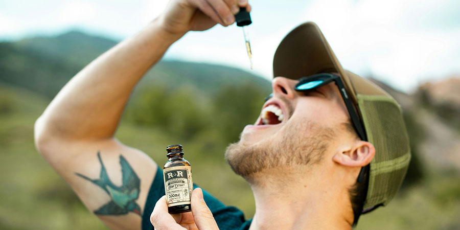 man holding a dropper taking a hemp extract CBD oil while holding a small bottle with his other hand